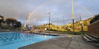 Glassell Pool after a raining day with a full rainbow in the sky with Lifeguard on tower and coaches teaching a class.